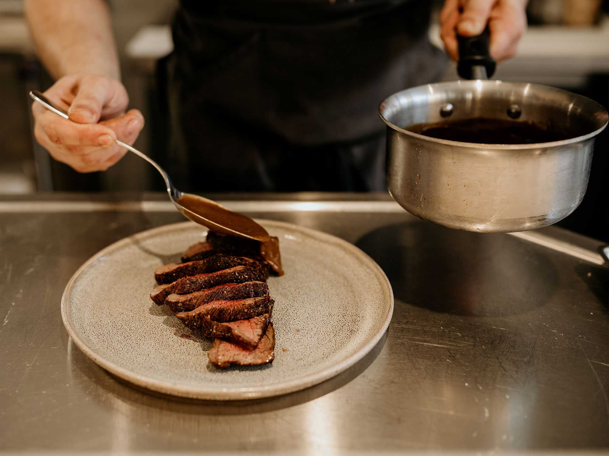 A tight shot of the chef ladling a sauce over a sliced steak. Photo is from our chattanooga photography marketing package.